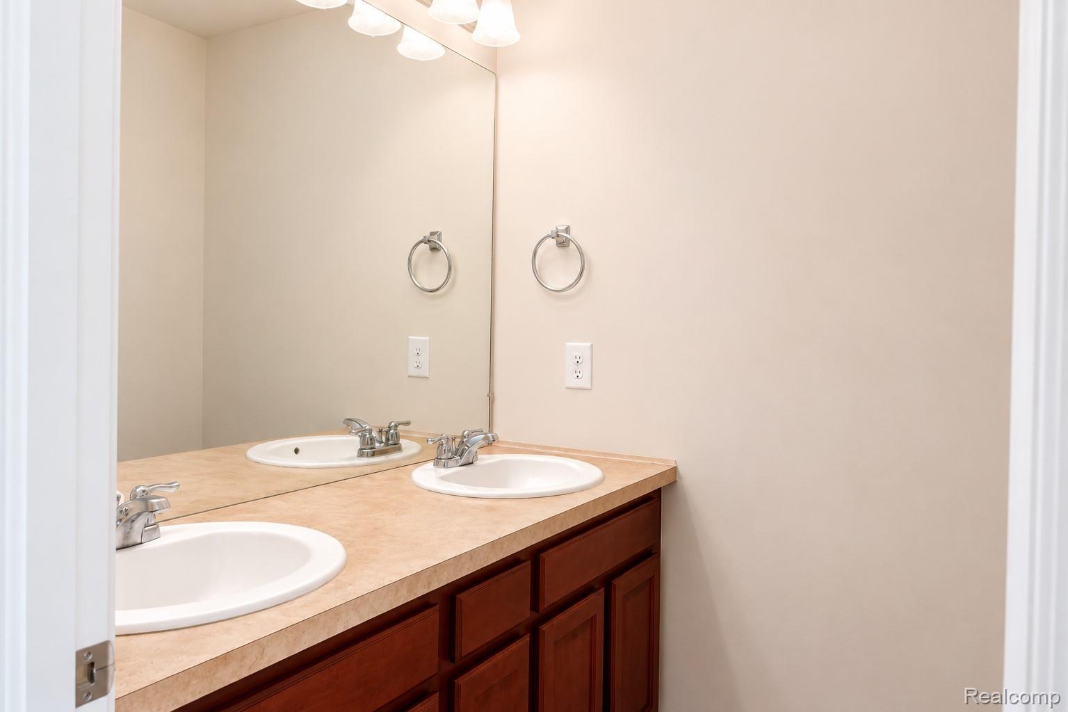 2940 Glenbar Circle Rochester, MI 48307 - Photo 10 of 15 Double vanity featuring two undermount sinks with chrome faucets, a light-toned countertop, and rich wood-finish cabinetry