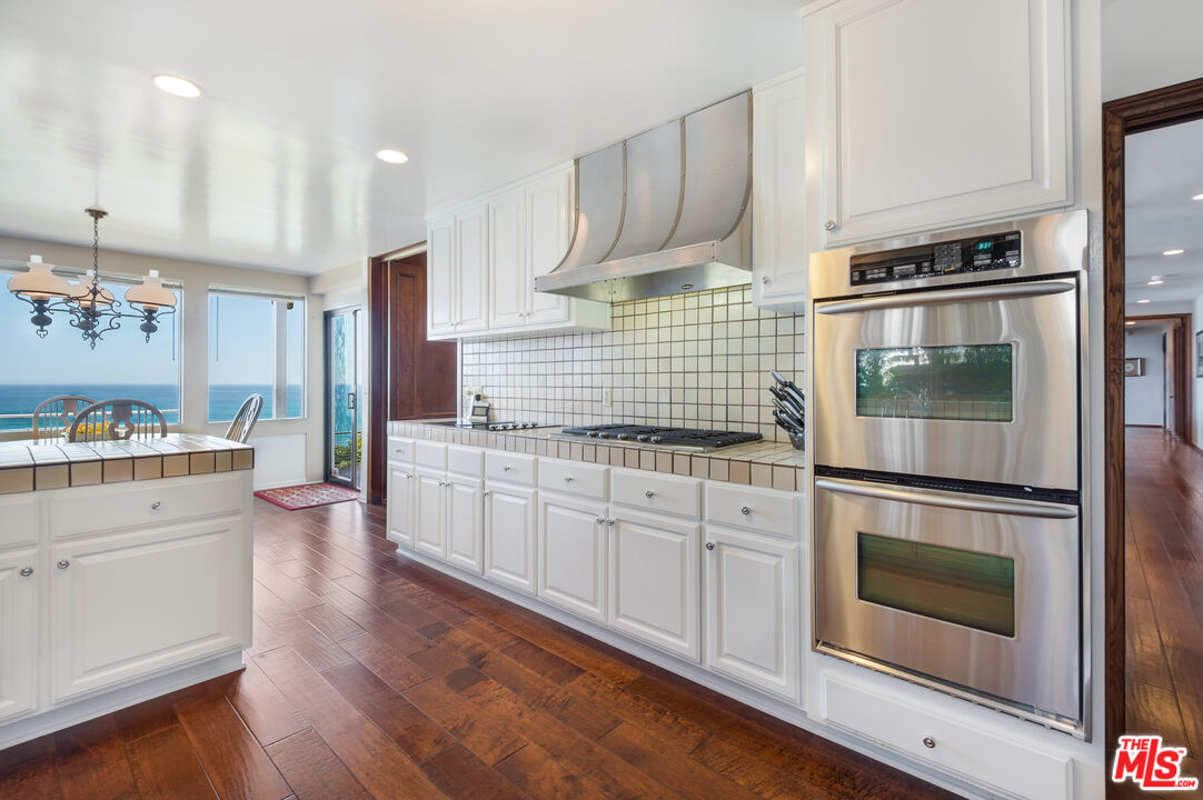 29008 Cliffside Drive Malibu, CA 90265 - Photo 8 of 28 a kitchen with stainless steel appliances white cabinets and wooden floors