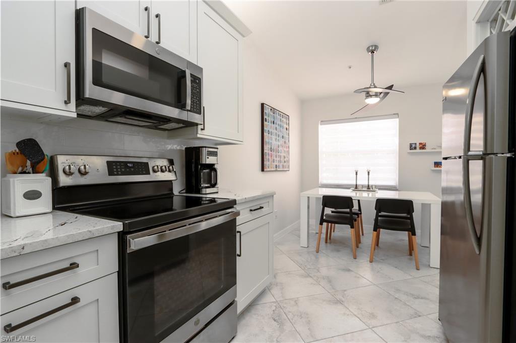 2585 Old Groves Road, Unit L203 Naples, FL 34109 - Photo 6 of 21 Kitchen with stainless steel appliances, light marble finish flooring, light stone countertops, and white cabinets