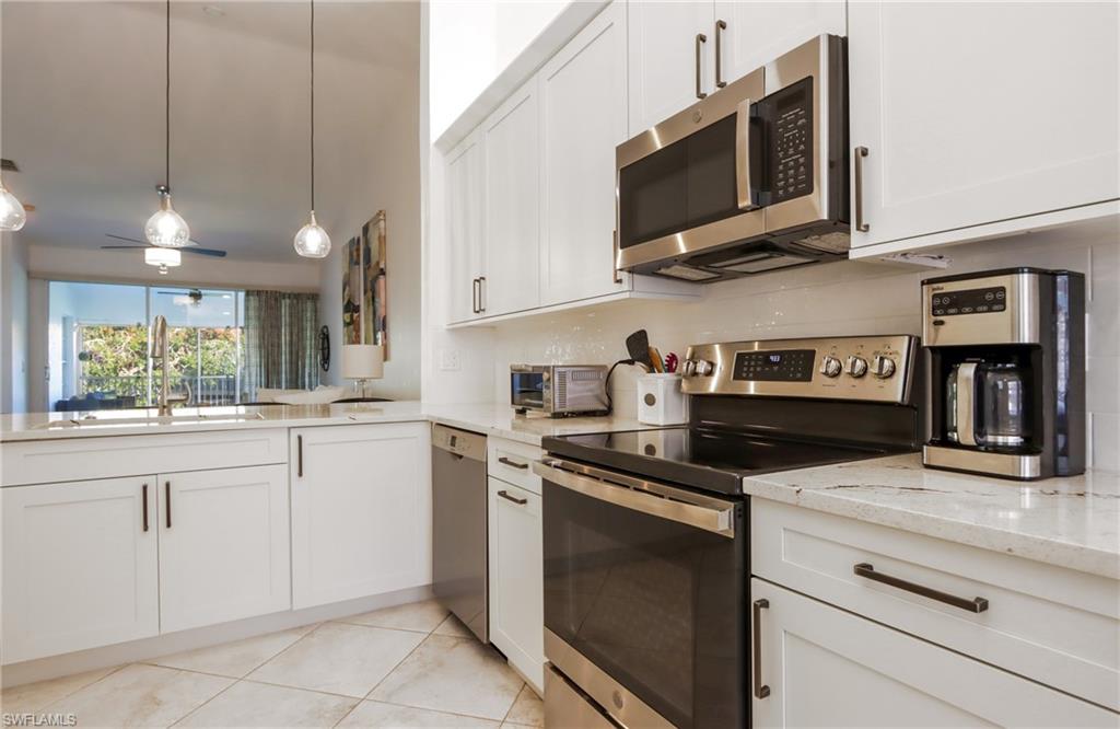 2585 Old Groves Road, Unit L203 Naples, FL 34109 - Photo 7 of 21 Kitchen with appliances with stainless steel finishes, light stone counters, white cabinets, light tile patterned floors, and decorative light fixtures