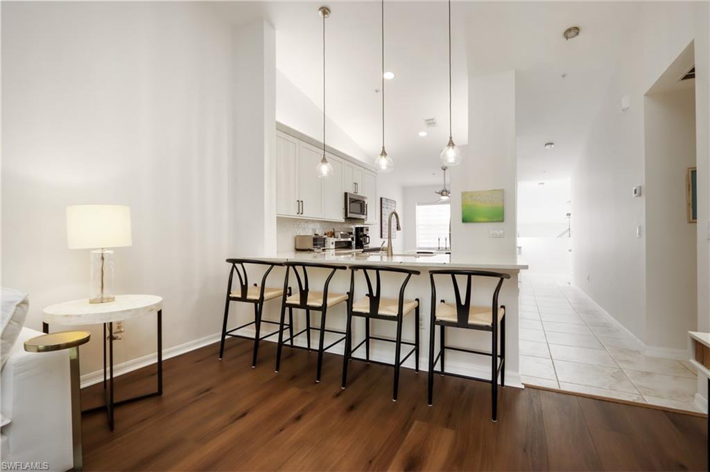 2585 Old Groves Road, Unit L203 Naples, FL 34109 - Photo 8 of 21 Kitchen with stainless steel microwave, white cabinets, a kitchen bar, a peninsula, and light wood-style floors
