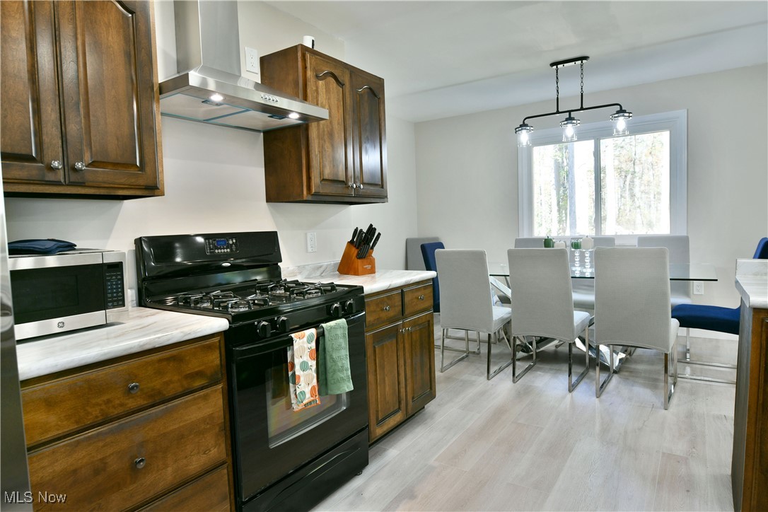 9633 Howland Springs Road Southeast Warren, OH 44484 - Photo 24 of 50 Kitchen with black gas range, wall chimney range hood, light countertops, stainless steel microwave, and hanging light fixtures