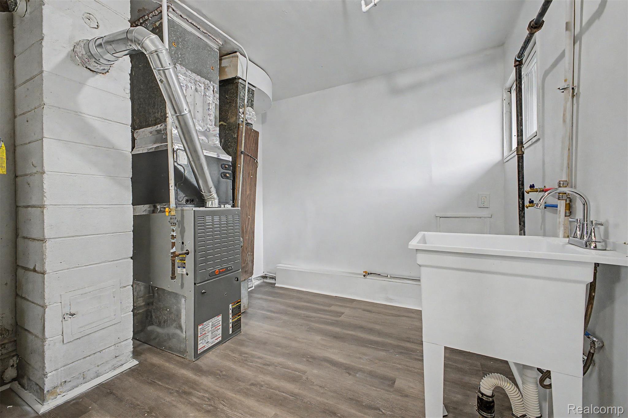 26718 Penn Street Inkster, MI 48141 - Photo 10 of 27 Utility area featuring a modern furnace system, wood-finish flooring, a utility sink with a chrome faucet, and white painted walls