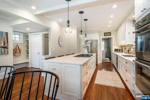 a kitchen with stainless steel appliances kitchen island granite countertop a stove a sink a refrigerator and white cabinets with wooden floor