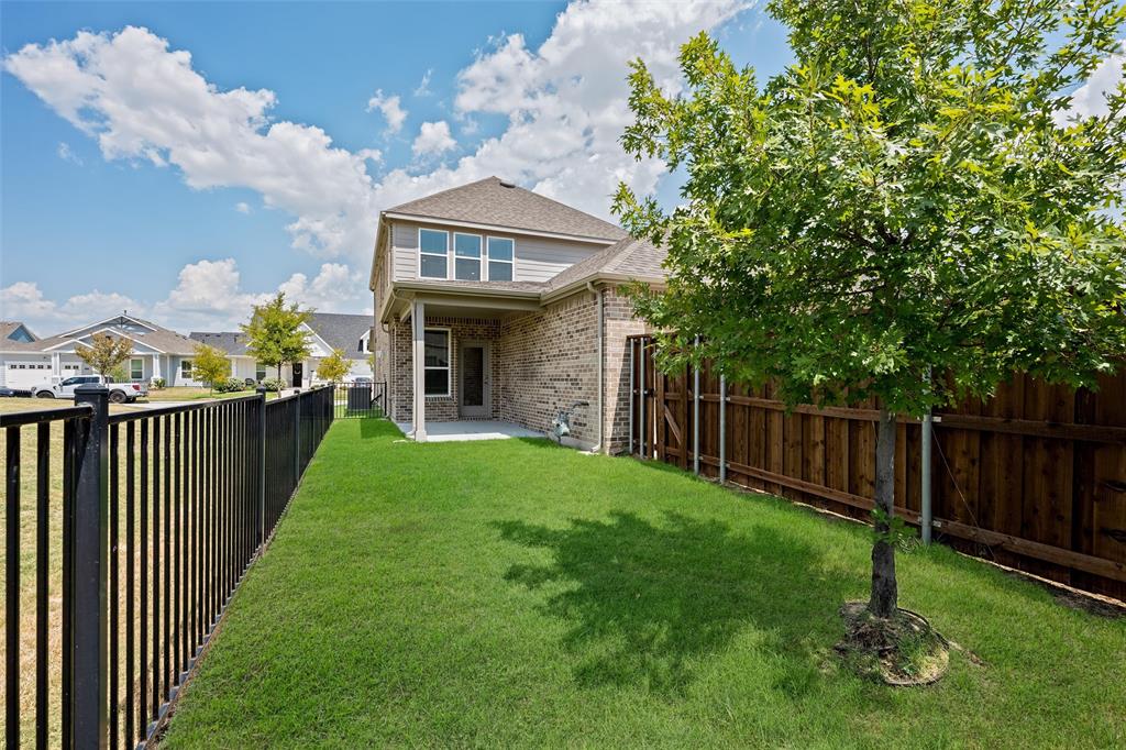 8715 Royal Star Road Rowlett, TX 75089 - Photo 34 of 39 Expansive backyard featuring a manicured lawn, a young tree, a black metal fence, a wooden privacy fence, and a covered patio area