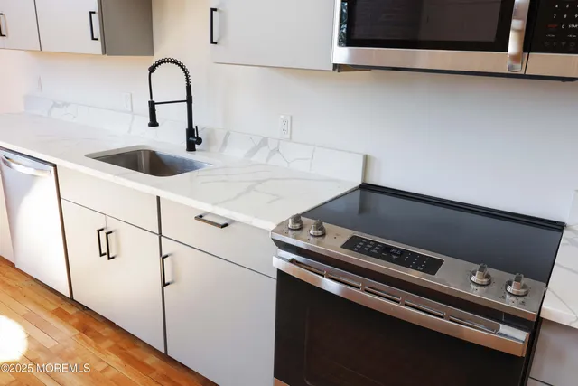 a large kitchen with stainless steel appliances granite countertop a stove a sink dishwasher a refrigerator and white cabinets with wooden floor