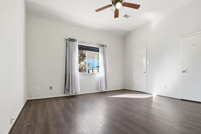 an empty room with wooden floor chandelier fan and windows