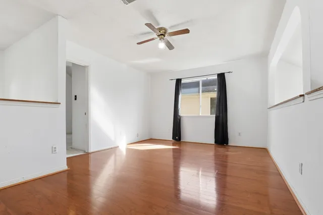 a view of an empty room with wooden floor and a ceiling fan