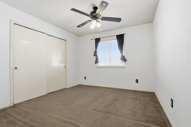 an empty room with chandelier fan and windows