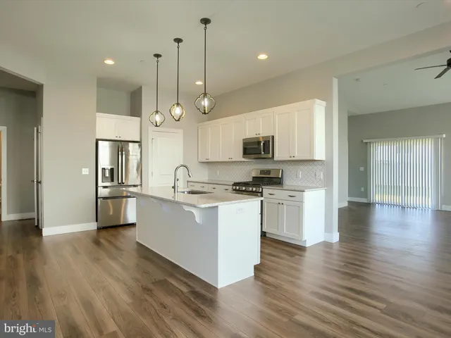 a kitchen with stainless steel appliances kitchen island granite countertop a refrigerator a oven a stove and white cabinets with wooden floor