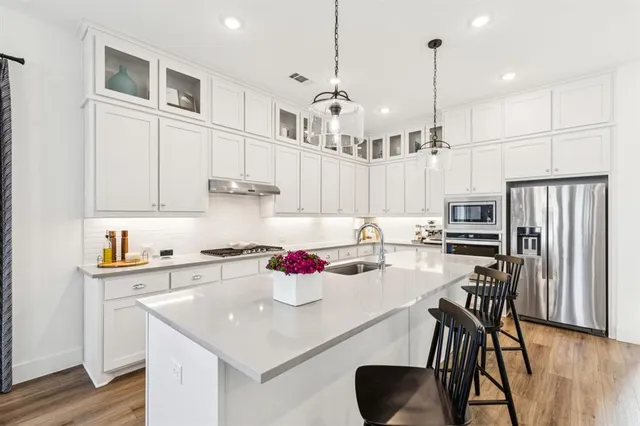 a kitchen with stainless steel appliances granite countertop a stove a refrigerator a sink a dining table and chairs with wooden floor