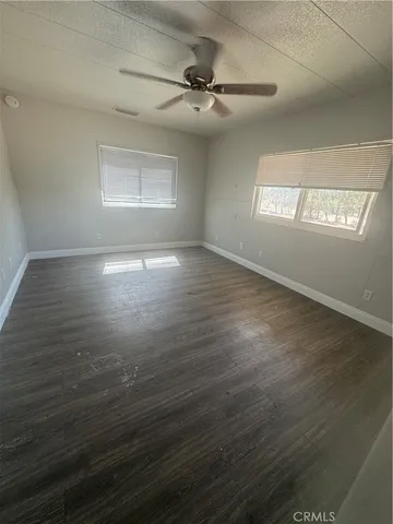 an empty room with wooden floor fan and windows