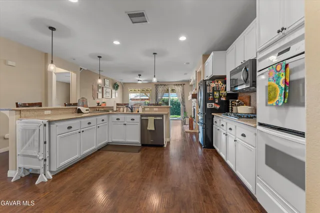 a kitchen with stainless steel appliances granite countertop a refrigerator a oven a stove and white cabinets with wooden floor