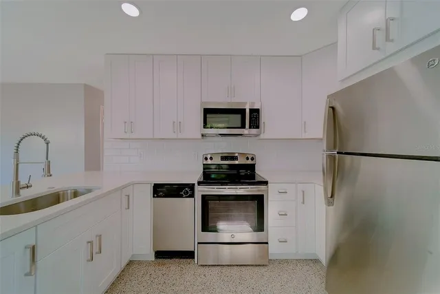 a view of kitchen with stainless steel appliances granite countertop a refrigerator a sink a stove and a refrigerator with wooden floor