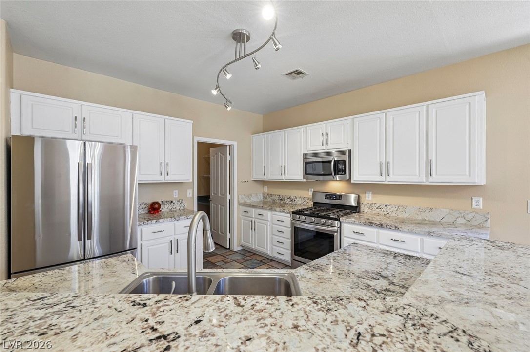 1727 Millstream Way Henderson, NV 89074 - Photo 16 of 46 White cabinetry and stainless steel appliances complete this well-equipped kitchen with stone countertops.
