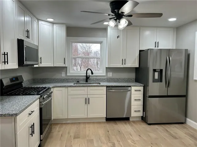 a kitchen with stainless steel appliances granite countertop a sink a stove a refrigerator a microwave oven with white cabinets