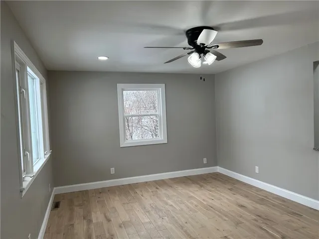 an empty room with wooden floor fan and windows
