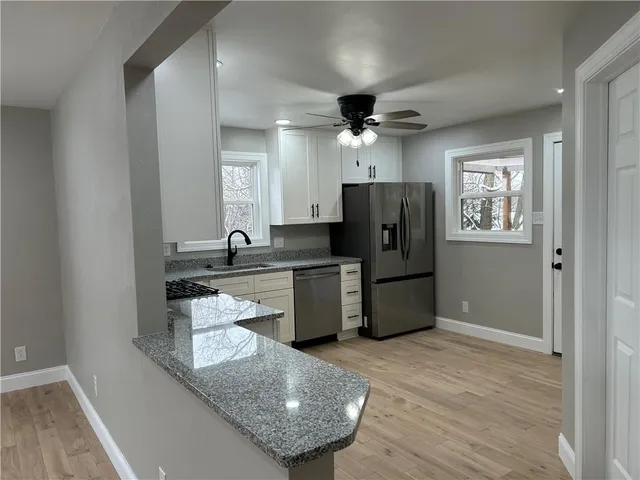 a large kitchen with granite countertop a refrigerator a sink dishwasher a stove and white countertops with wooden floor