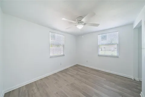 an empty room with wooden floor ceiling fan and windows