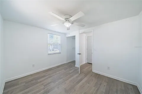 a view of an empty room with wooden floor and a ceiling fan