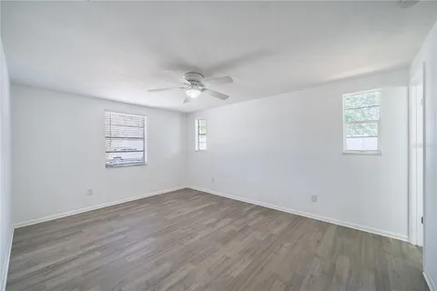 an empty room with wooden floor chandelier fan and windows