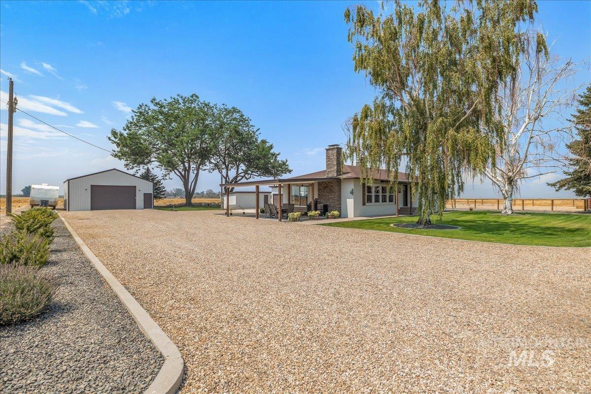 23011 Allendale Road Parma, ID 83660 - Photo 3 of 50 Expansive gravel driveway, detached metal-sided garage, covered patio, stone-clad chimney, and mature trees