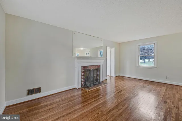 an empty room with wooden floor fireplace and windows