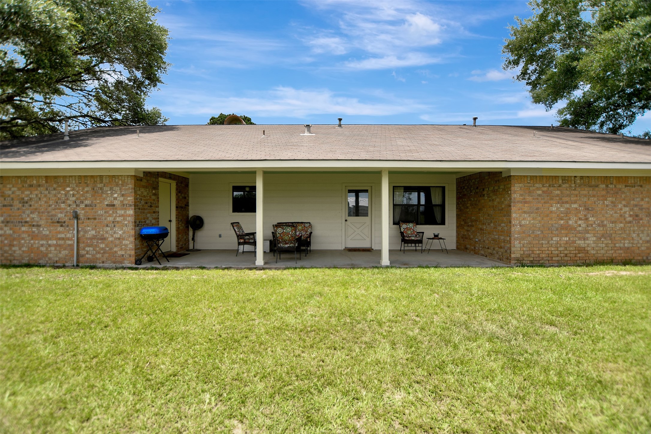 341 South S Loop Bellville, TX 77418 - Photo 28 of 33 This photo features the back view of a single-story brick home with a spacious covered patio, ideal for outdoor relaxation. The yard is large and grassy, perfect for activities or gardening.