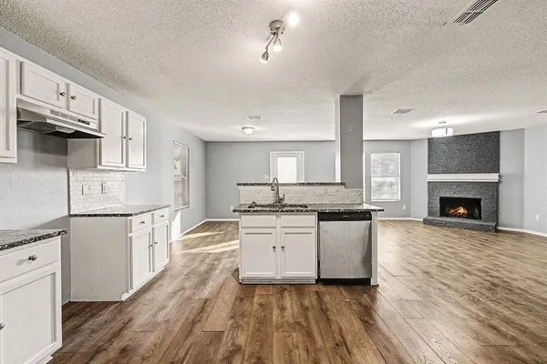 a kitchen with granite countertop a stove top oven a sink dishwasher and a fireplace with wooden floor