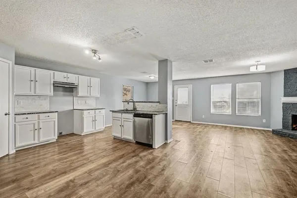 a large kitchen with a stove a sink dishwasher a refrigerator and white cabinets with wooden floor