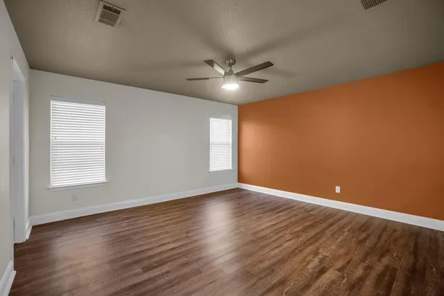 an empty room with wooden floor ceiling fan and windows