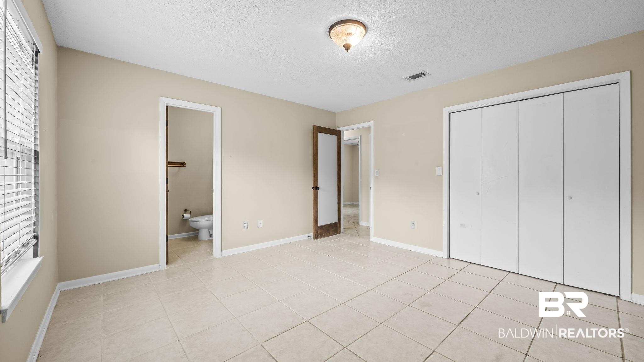 15096 Highland Circle Foley, AL 36535 - Photo 27 of 52 Spacious room featuring neutral-toned walls, cream-colored tile flooring, window with blinds, bi-fold closet doors, and a ceiling-mounted light fixture