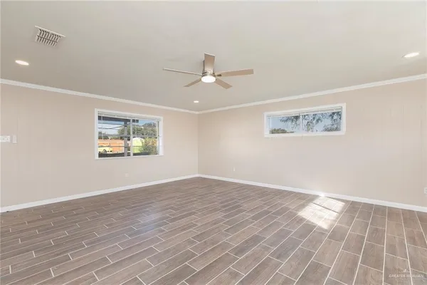 an empty room with wooden floor chandelier fan and windows