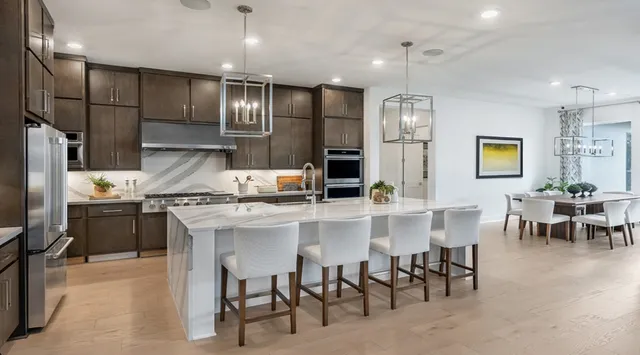 a kitchen with stainless steel appliances kitchen island granite countertop a table chairs refrigerator and microwave