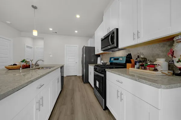 a kitchen with stainless steel appliances kitchen island granite countertop a dining table chairs and a refrigerator