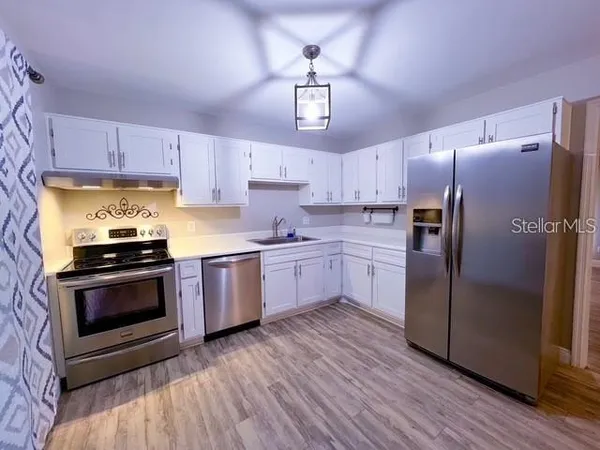 a kitchen with stainless steel appliances a stove a sink dishwasher a refrigerator and a stove with wooden floor