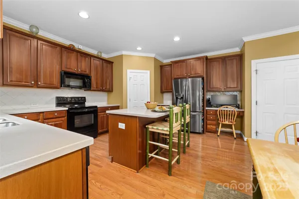 a kitchen with stainless steel appliances a stove a sink a microwave a refrigerator a dining table and chairs with wooden floor