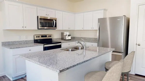 a kitchen with stainless steel appliances granite countertop a sink a microwave a refrigerator and white cabinets