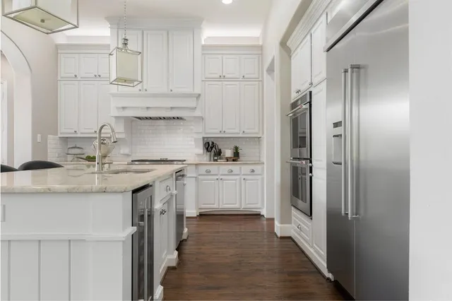 a kitchen with stainless steel appliances granite countertop a refrigerator a sink dishwasher and white cabinets with wooden floor