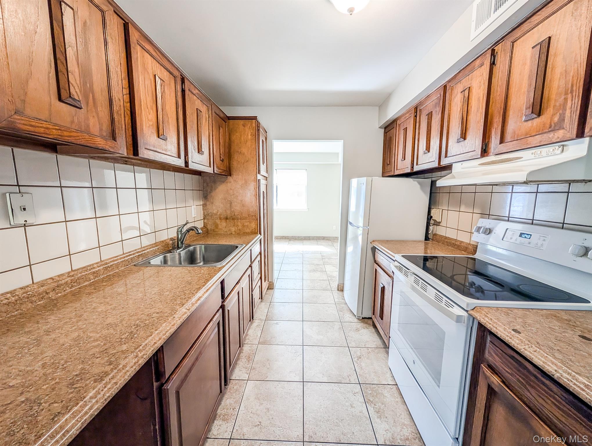 136 Hill Crescent Calverton, NY 11933 - Photo 2 of 21 Kitchen with white electric range oven, tasteful backsplash, under cabinet range hood, light tile patterned floors, and brown cabinetry