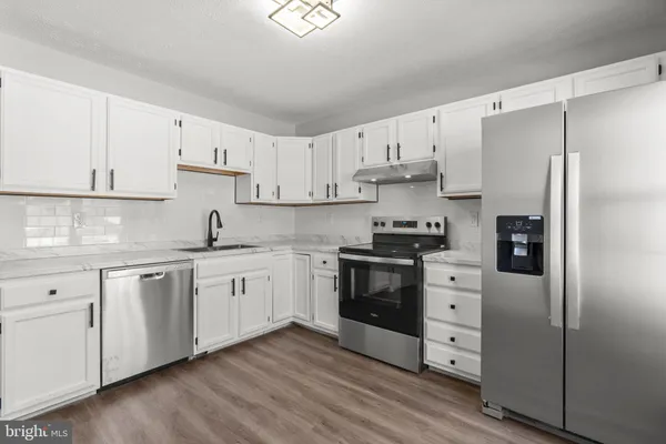 a kitchen with granite countertop a refrigerator stove and white cabinets