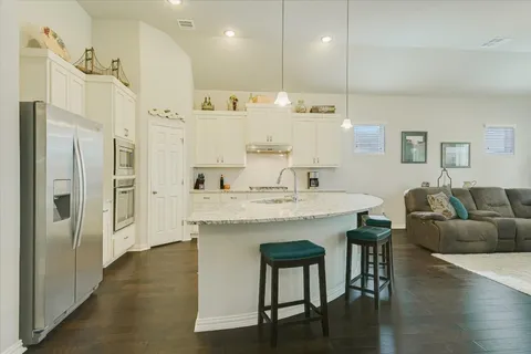 a kitchen with stainless steel appliances kitchen island granite countertop a refrigerator a stove a sink and white cabinets with wooden floor