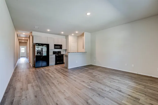 an empty room with wooden floor and kitchen