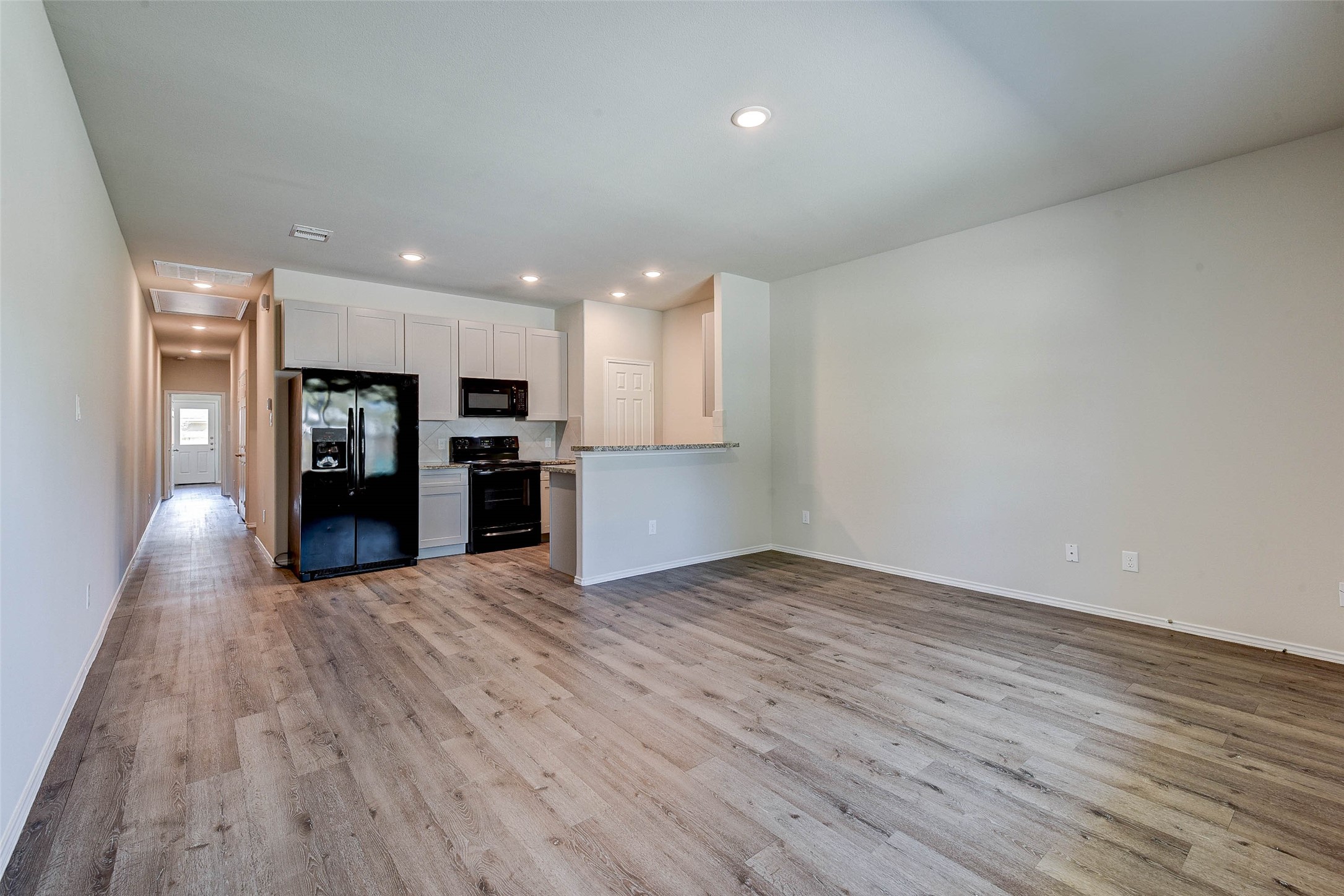 409 East Avenue G Conroe, TX 77301 - Photo 6 of 22 an empty room with wooden floor and kitchen