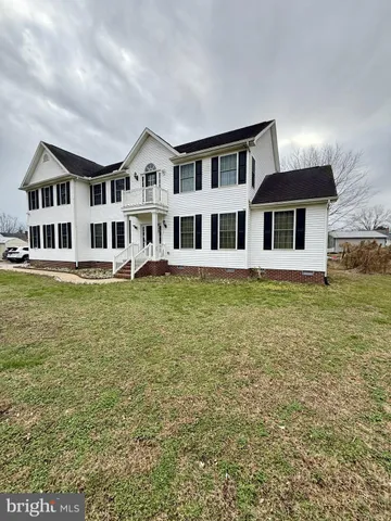 a large white building with a swimming pool and lawn chairs under an umbrella