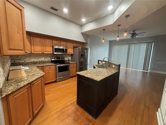 a kitchen with stainless steel appliances granite countertop a stove top oven a sink dishwasher and a refrigerator with wooden floor