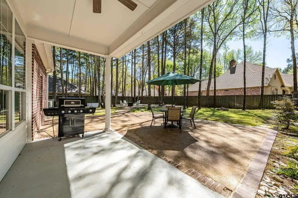 a view of a patio with table and chairs under an umbrella with large trees