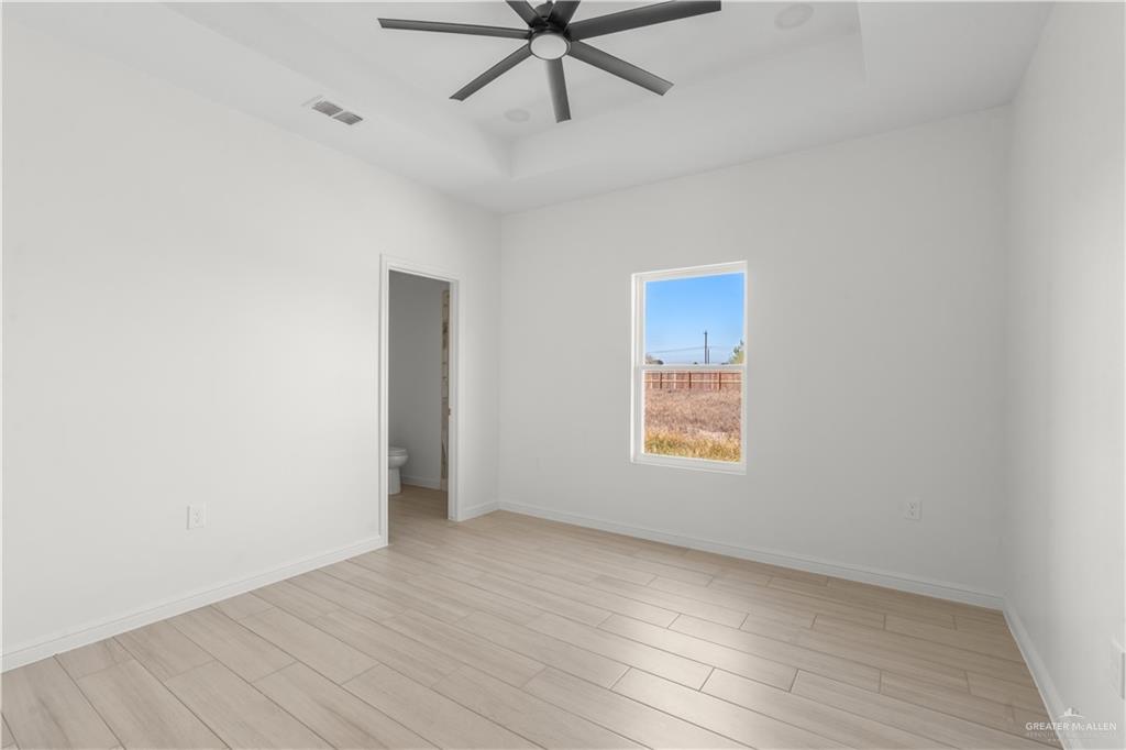 311 Other Road Rio Grande City, TX 78582 - Photo 12 of 16 Empty room with a tray ceiling, light wood-type flooring, and ceiling fan