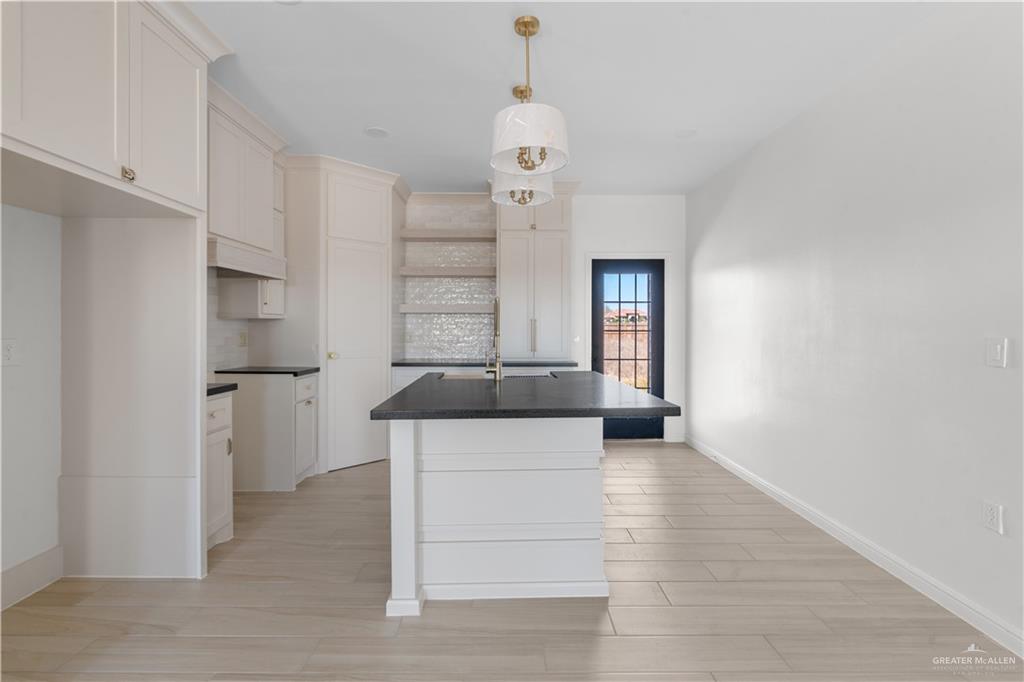 311 Other Road Rio Grande City, TX 78582 - Photo 3 of 16 Kitchen featuring a kitchen island with farm sink, dark countertops, light wood-type flooring, tasteful backsplash, and decorative light fixtures