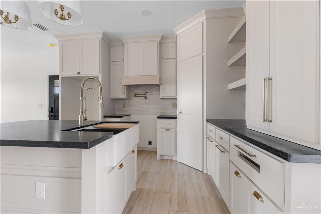 311 Other Road Rio Grande City, TX 78582 - Photo 5 of 16 Kitchen featuring open shelves, light wood-style floors, a center island with sink, backsplash, and dark stone countertops